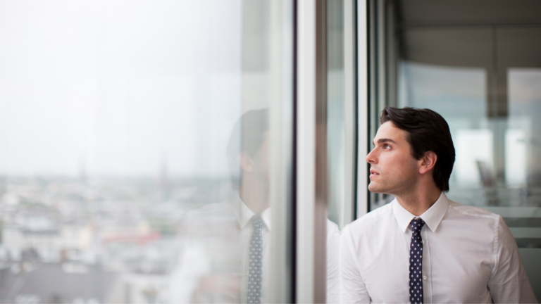 High achieving senior leader looking out office window feeling stuck even when everything looks right.