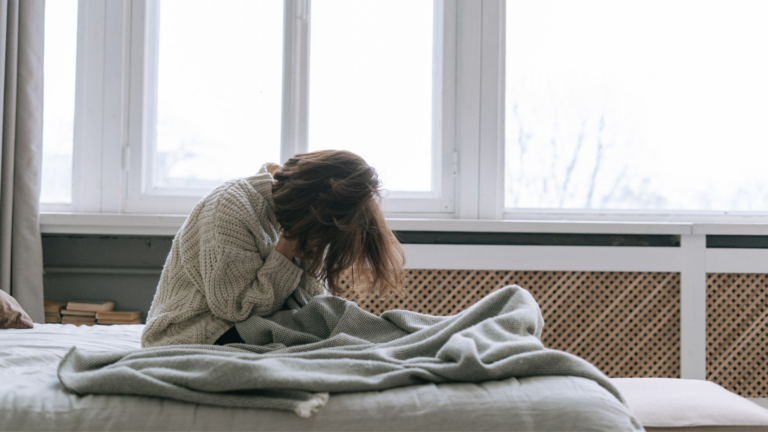 Person sitting on a bed looking exhausted and overwhelmed, illustrating the feeling of being drained even after rest.