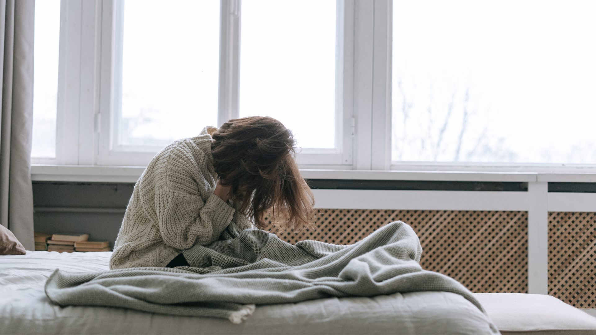 Person sitting on a bed looking exhausted and overwhelmed, illustrating the feeling of being drained even after rest.