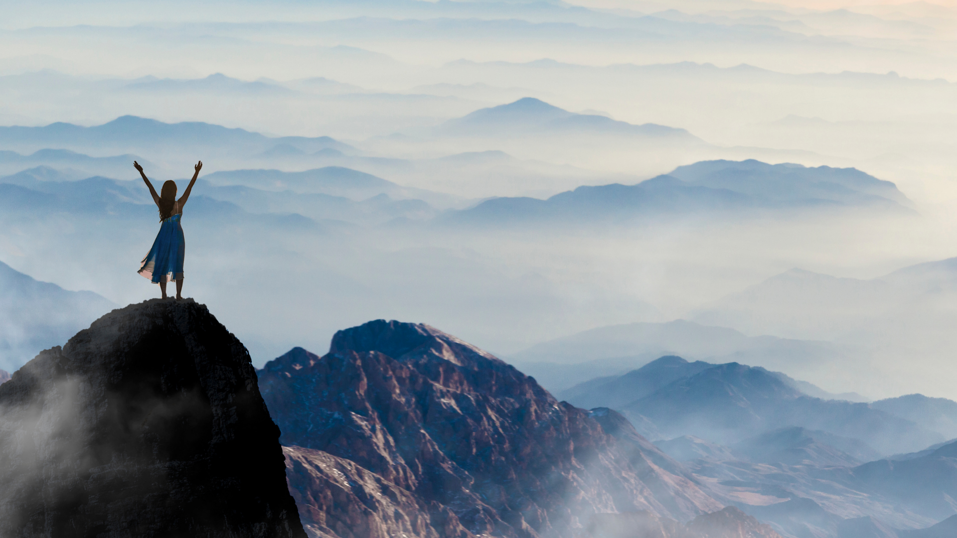 Woman standing on a mountain peak overlooking an expansive landscape, representing feeling called to more and new possibilities.